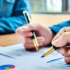 Hands holding pens working on documents